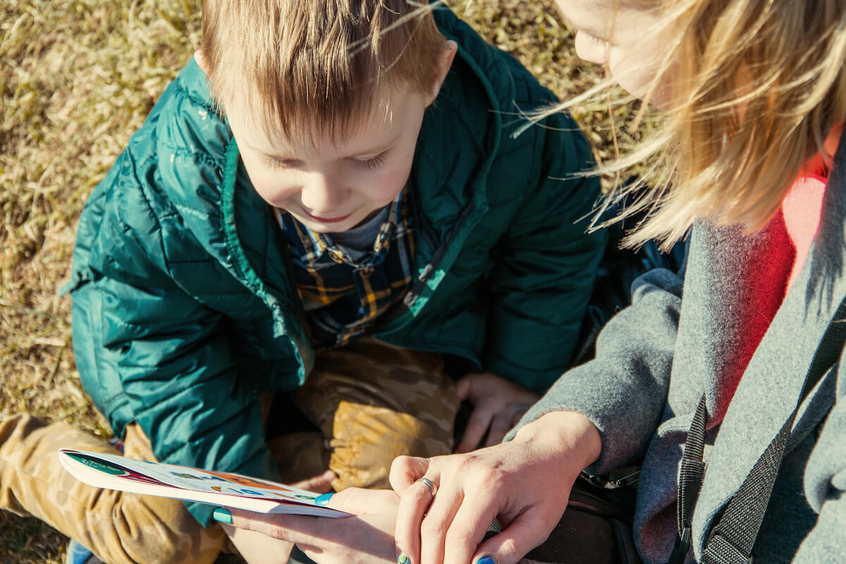two children reading a book outdoors wearing winter gear
