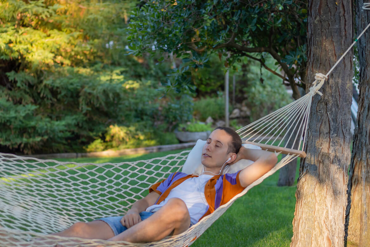 teenage boy relaxing in a hammock while camping with earpods in