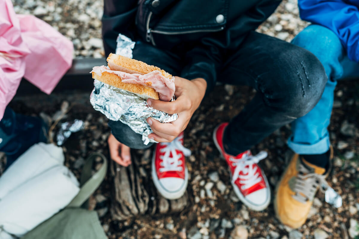 a group of people eating foil wrapped sandwiches for lunch while camping.