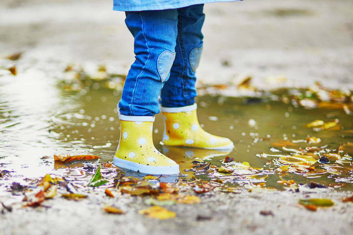 toddler wearing yellow gum boots and jeans splashing in a puddle