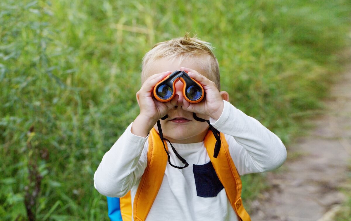 toddler boy looking through a pair of orange binoculars.