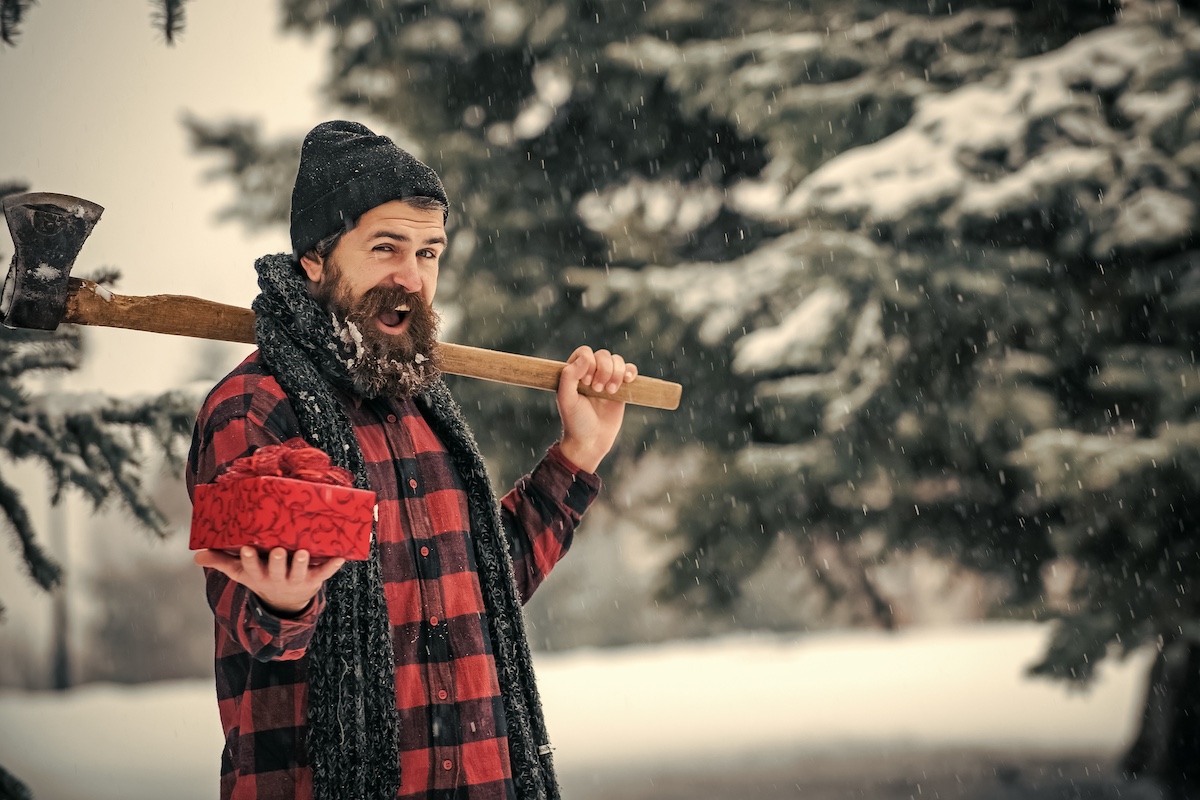 man walking through snowy field with axe over shoulder and christmas gift in his hand.