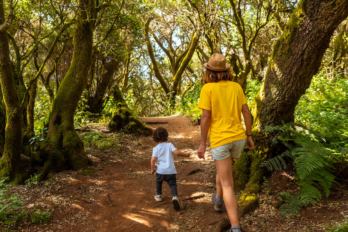 toddler wandering along nature trail followed by mother.