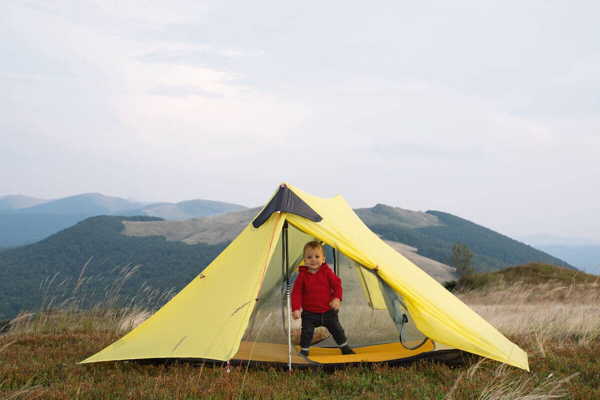 toddler standing inside the entrance of a yellow tent.