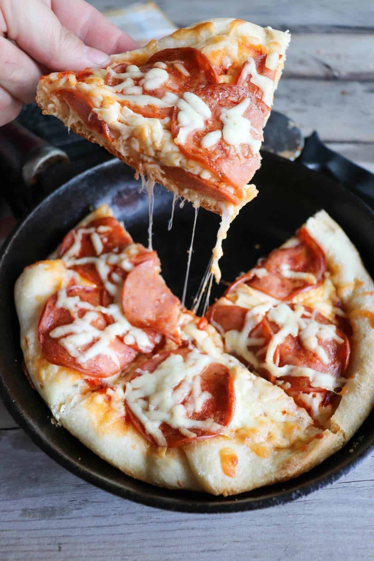 hand holding a slice of skillet pizza above the skillet.