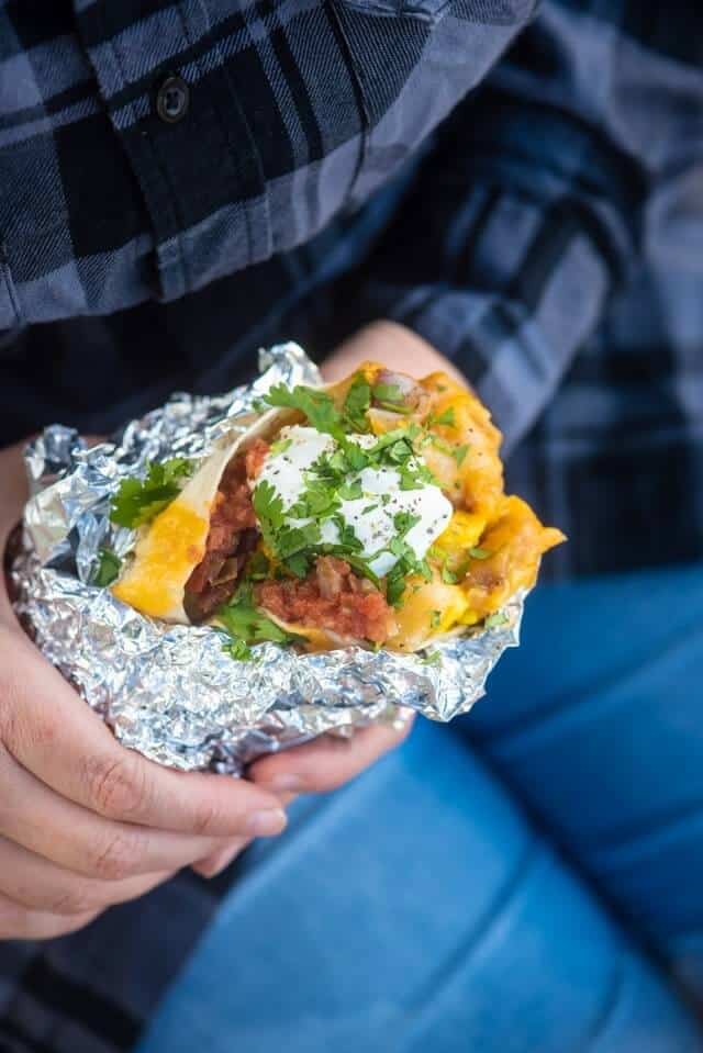 person holding a heated breakfast burrito wrapped in foil.