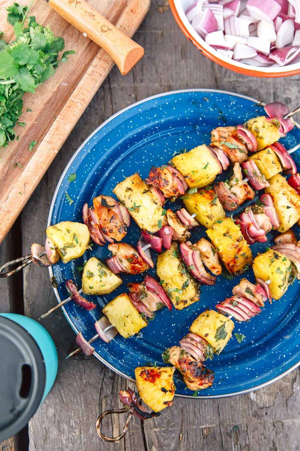 4 chicken and pineapple skewers on a large blew plate.
