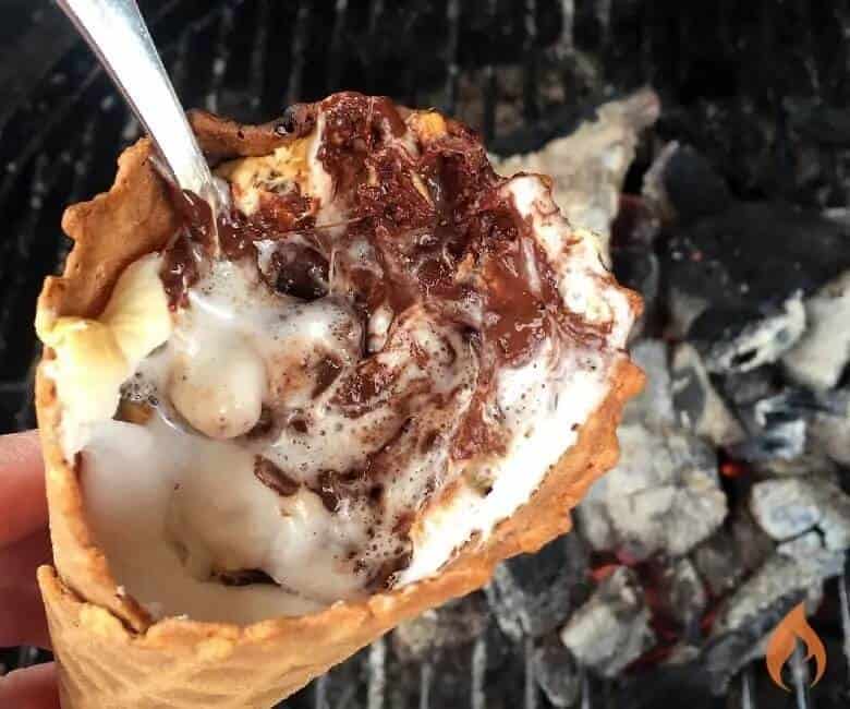 smores campfire cone with campfire coals in background and spoon sticking out of cone.