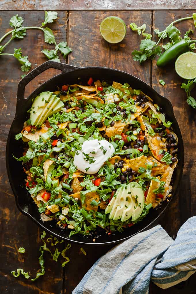 cast iron skillet with campfire nachos and extra ingredients scattered on wooden table.