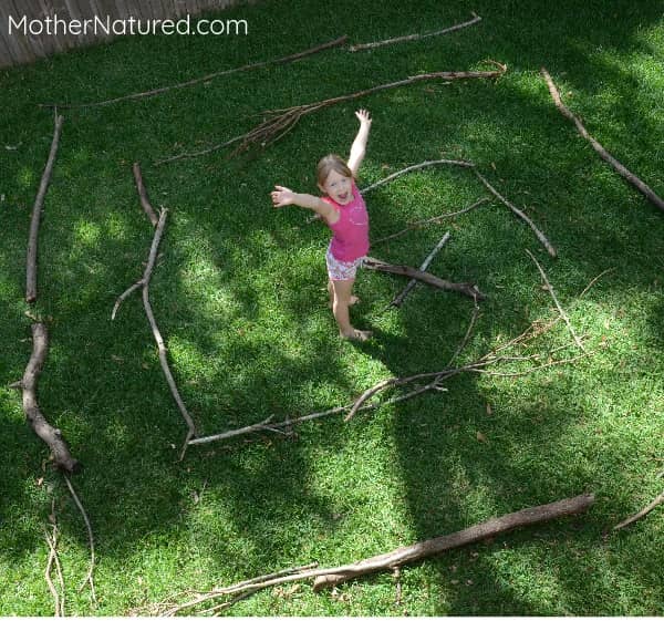 little girl in pink shirt standing in the middle of a maze made of sticks.
