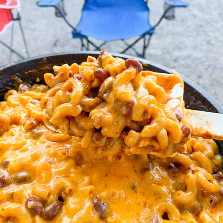 chili cheesy macaroni casserole in skillet with camping chairs in background.