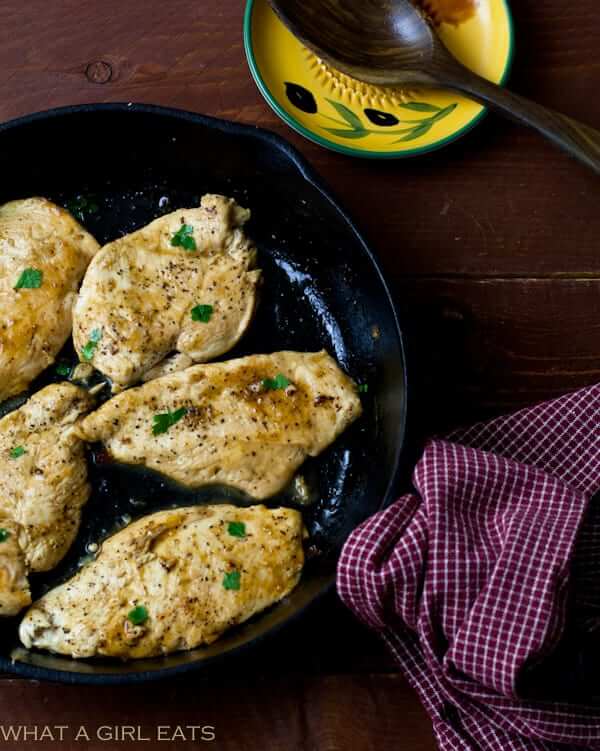 cast iron skillet with cooked chicken breasts on dark wood table.