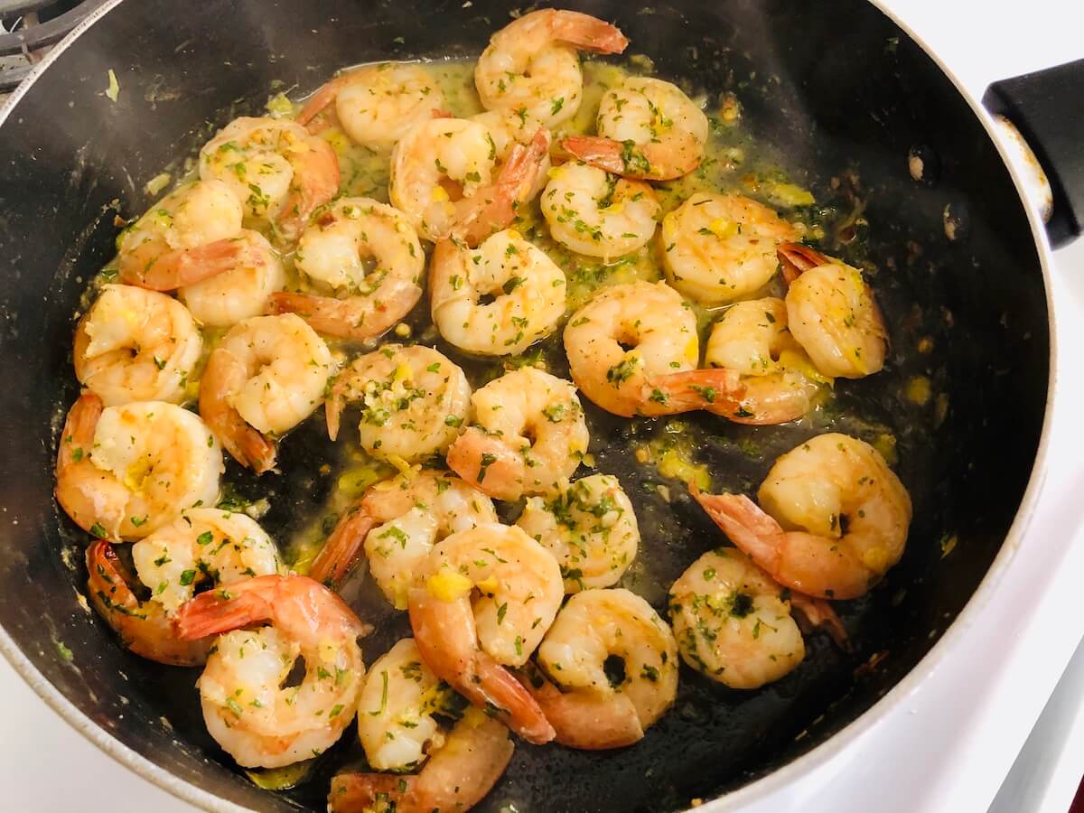 garlic prawns sizzling in pan with butter and herbs.