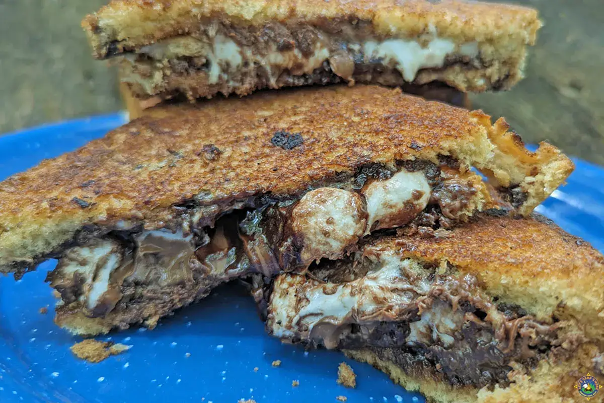 close up of grilled marshmallow smores sandwiches cut into halves on a blue plate.