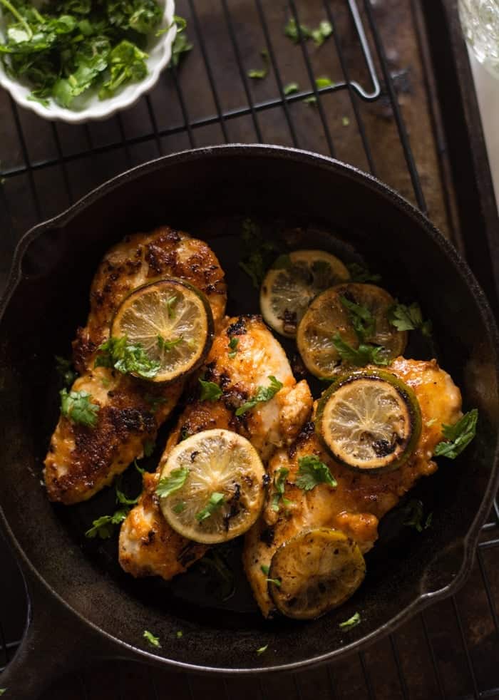 cooked chicken breasts with lime slices in a cast iron skillet on a wooden table.