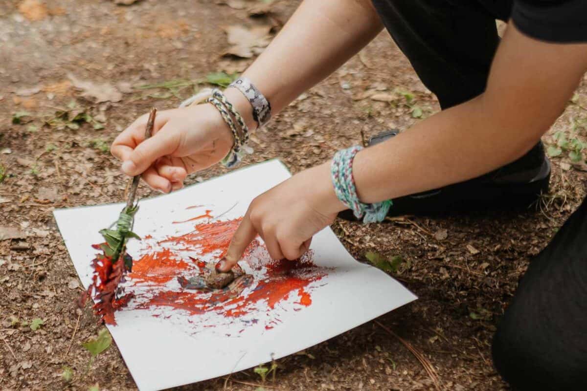 woman painting a piece of paper, using a leaf as a paint brush.