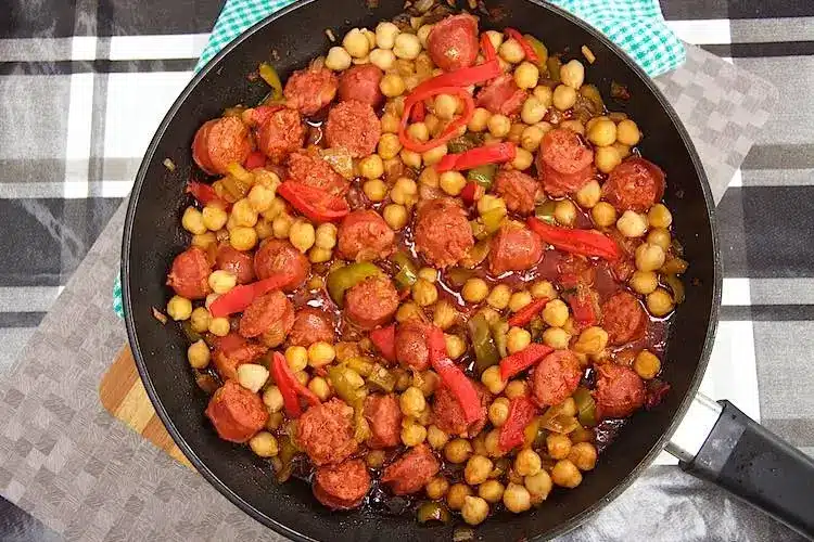 close up of cast iron skillet with chorizo chickpea meal on camping table.