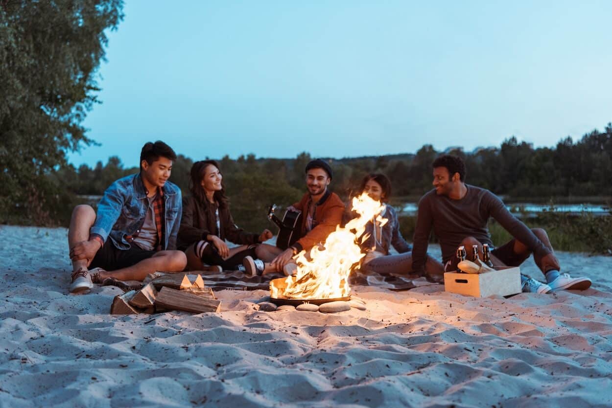 group of friends sitting around a beach campfire as the sun goes down.