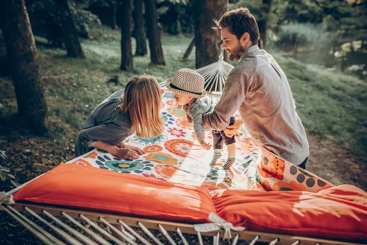 young parents with their baby leaning over a large hammock on a camping trip.