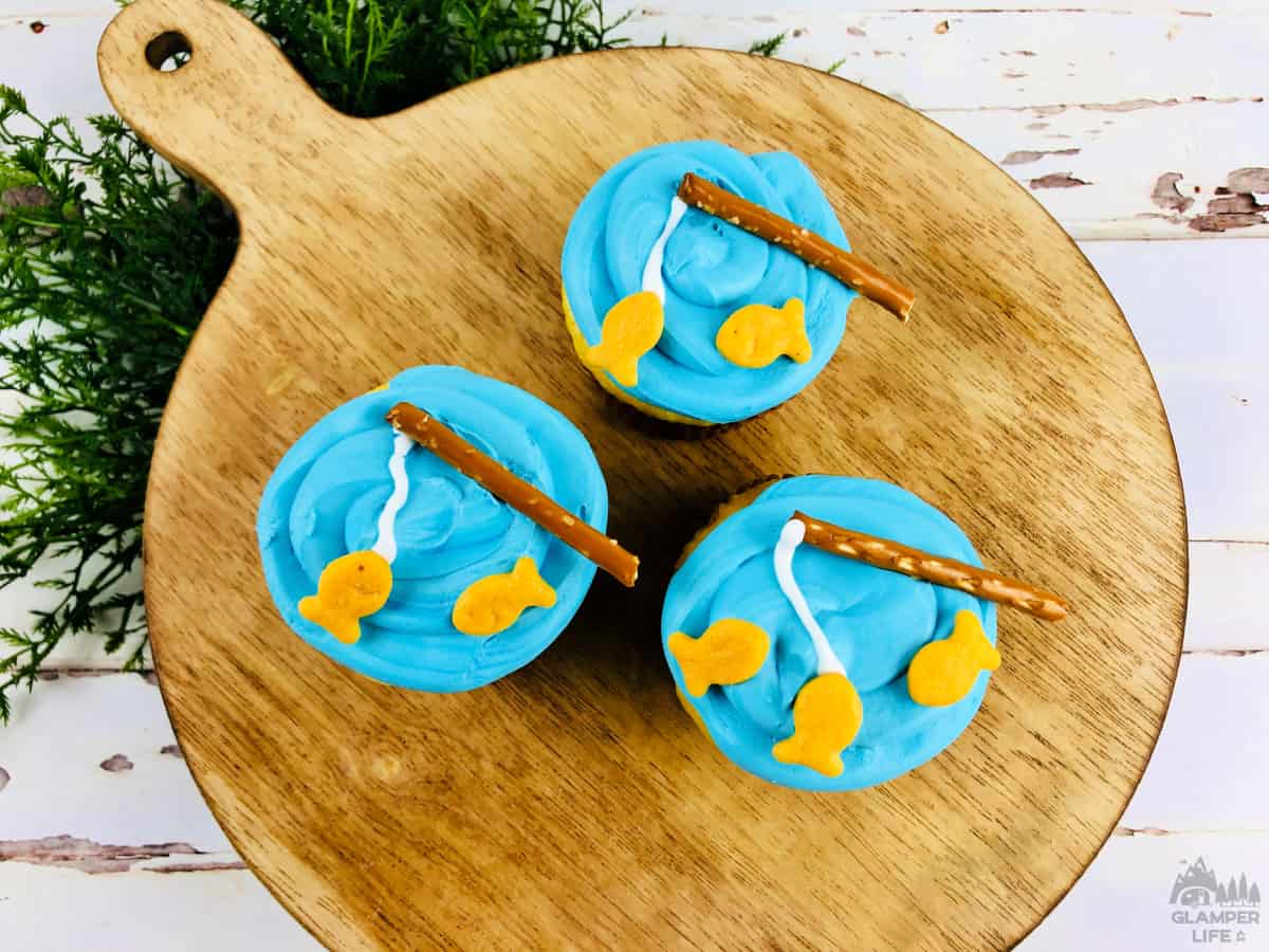 fishing cupcakes on a wooden serving board with blue icing and tiny fishing rods.