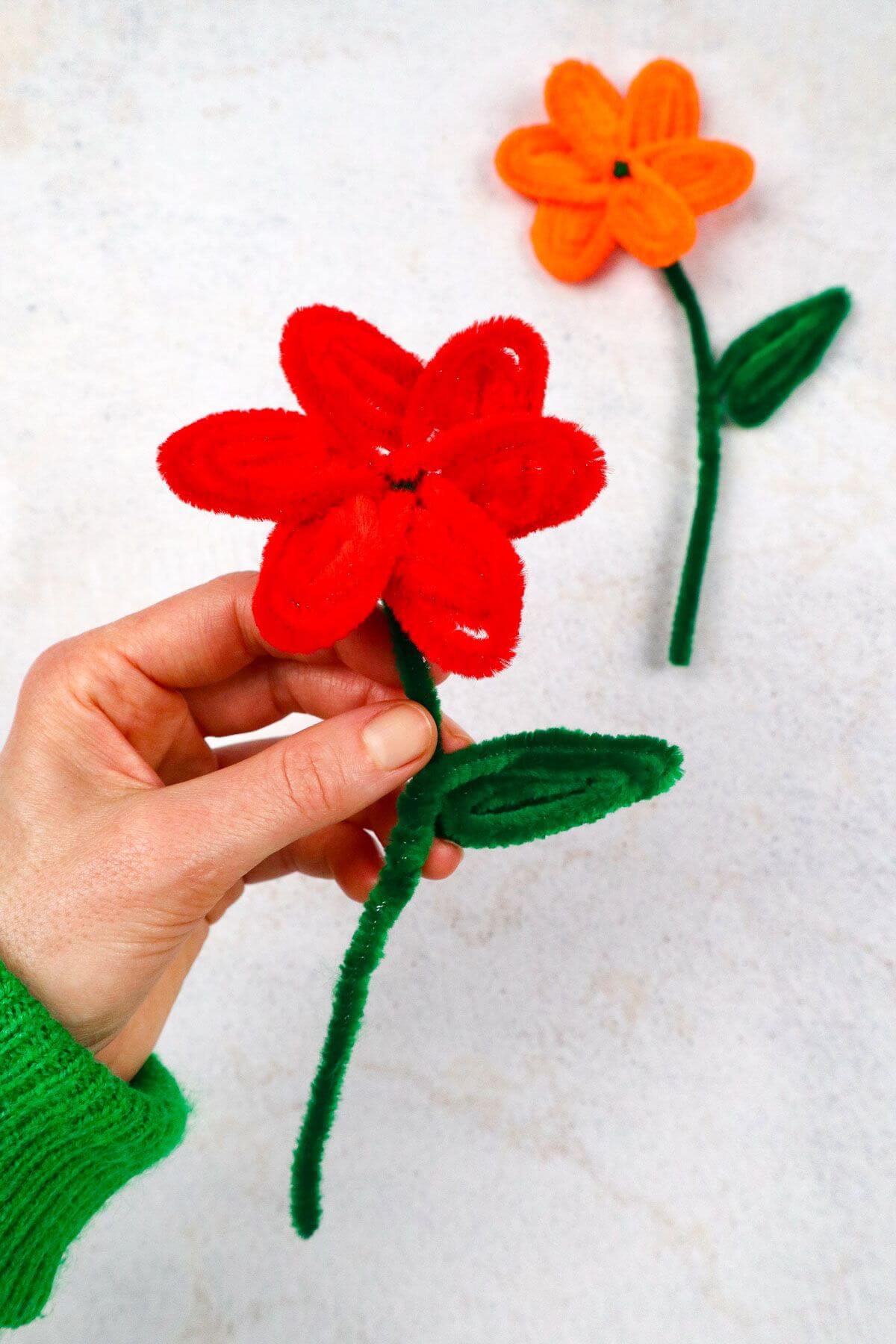 woman holding a red pipe cleaner flower with a second flower in the background.