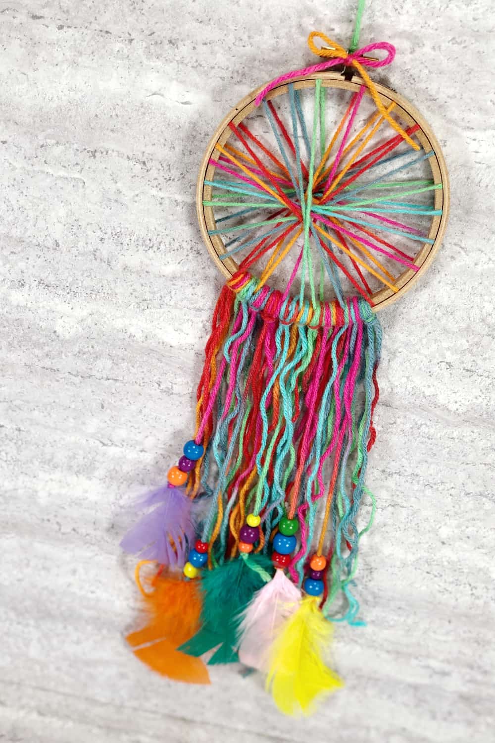 beautiful rainbow coloured dream catcher made with yarn and feathers.