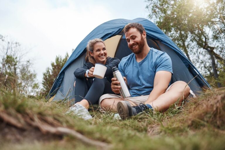 man and woman sitting in front of tent, laughing together.