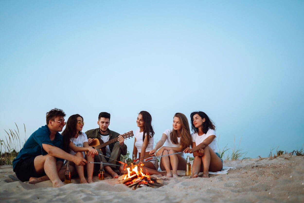 group of friends on a beach camping trip sitting around a campfire.