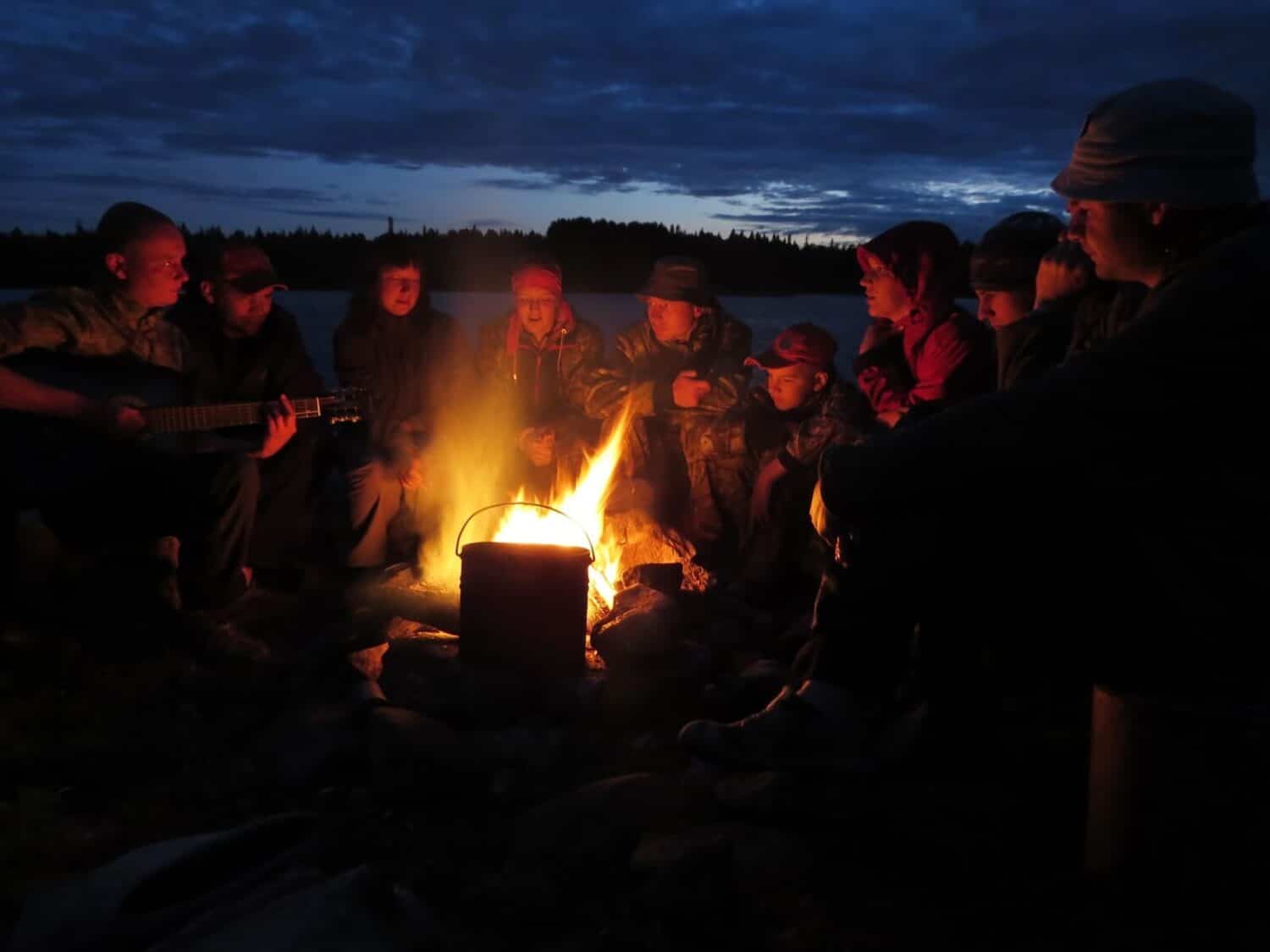 group of people sitting around a campfire at night.