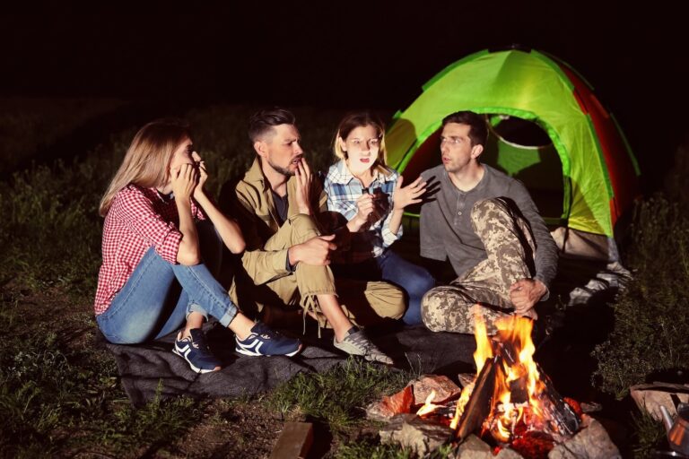 group of people sitting around campfire at night talking.