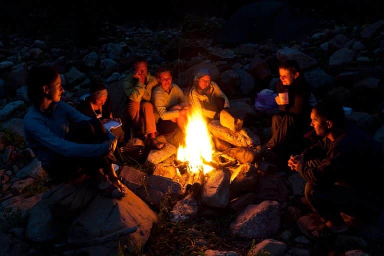 group of adults sitting around a campfire at night.