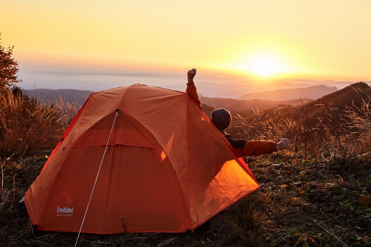 man stretching in front of orange tent at sunrise.